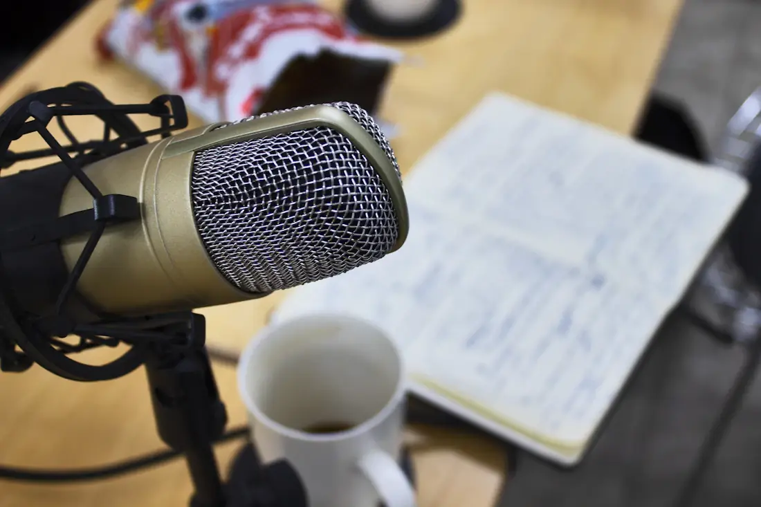 A studio condenser microphone beside an open notebook of handwritten pages on a wooden desk