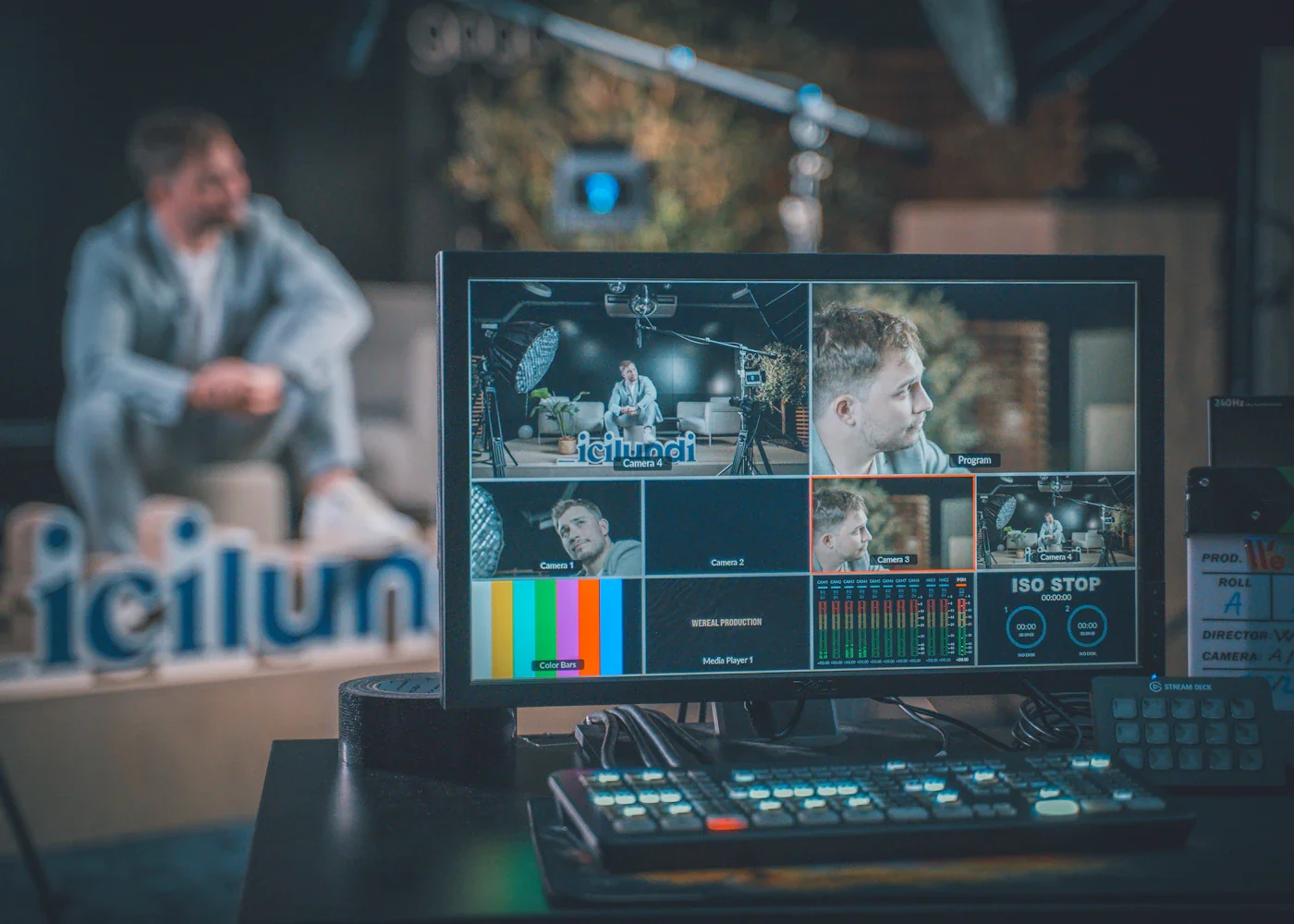 A broadcast control desk with monitors showing a live camera feed